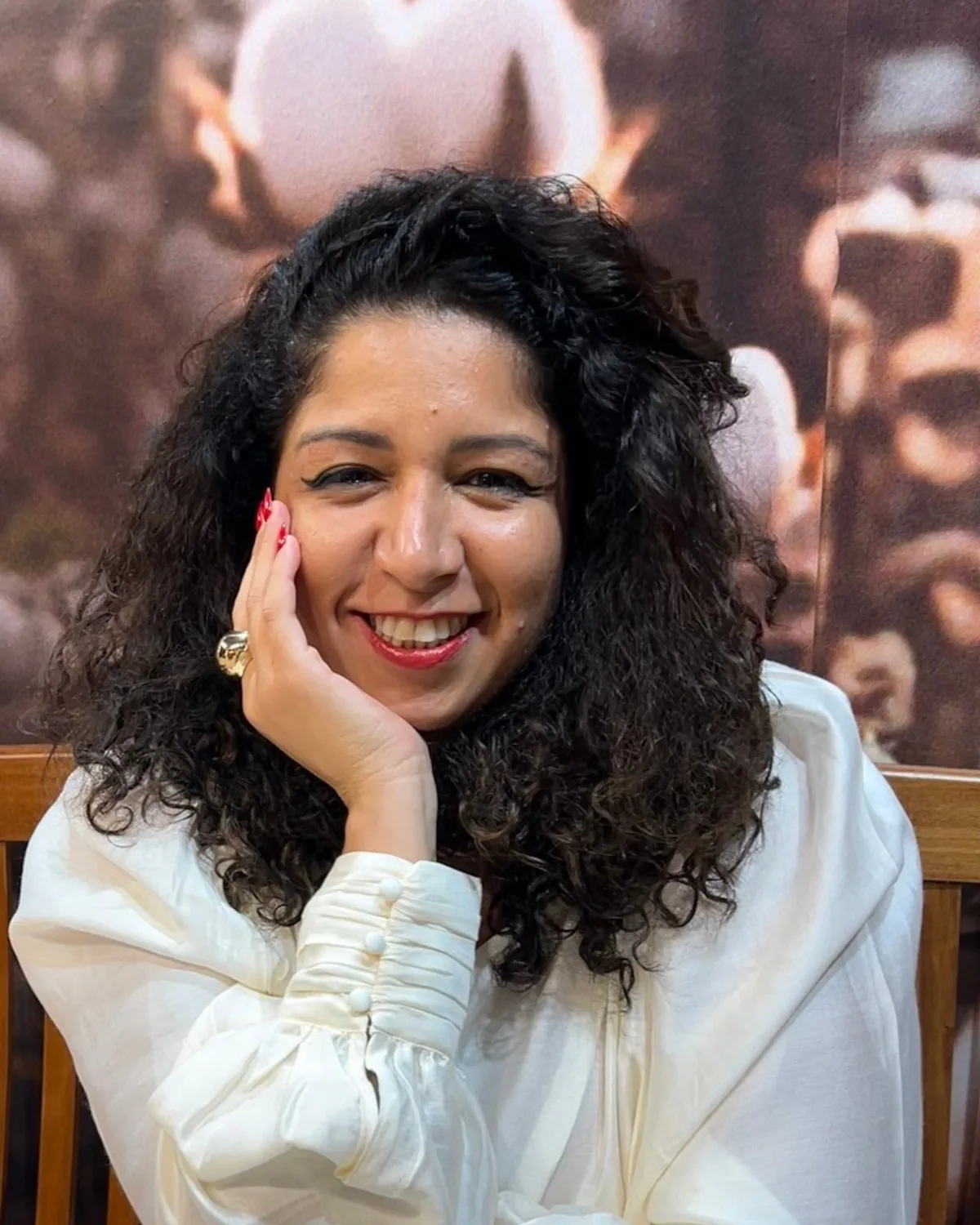 Priscila Ribeiro Campos, sentada num banco de madeira, sorrindo